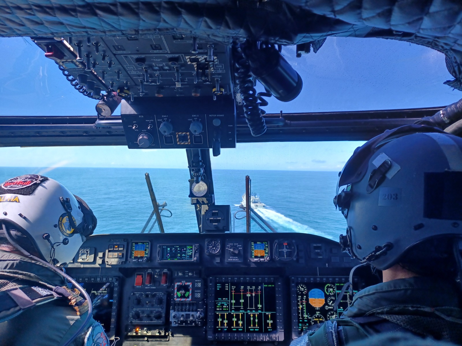 Dois pilotos de costas dentro cabine. O helicóptero está a voar